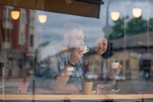 two friends drinking coffee in a cafe. Shot thought window with reflections.
