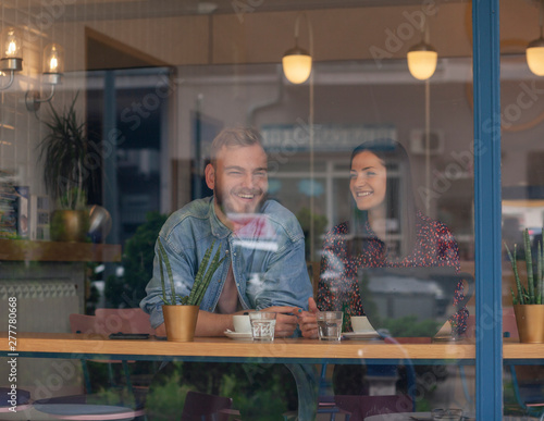 two friends talking in a cafe. Shot through window with street reflections.