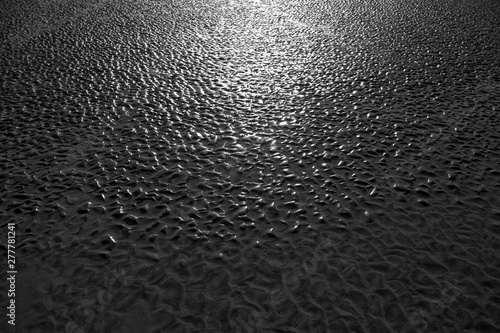 Natural background of wet textured sand with raised wave patterns shining in backlit sun on a beach at low tide