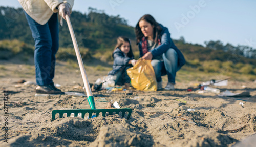 Closeup of rake with volunteer women cleaning the beach. Selective focus in rake in foreground