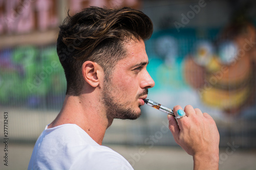 Handsome man smoking e-cigarette, vaping outdoor in city setting © theartofphoto