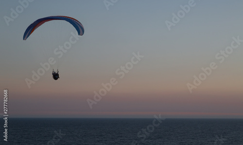 Silhouette of a paraglider flying over the waters of the baltic sea making use of the ridge lift over the cliffs at Kåseberga near Ystad, Sweden.