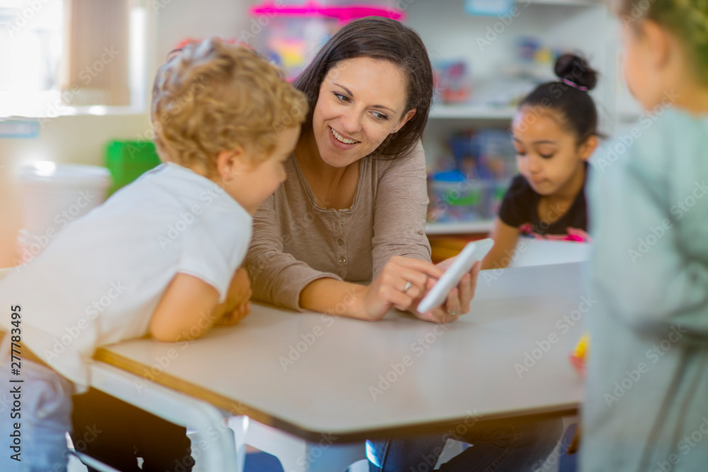 Pre-school teacher showing mini tablet to children in kindergarten Pre-school teacher showing mini tablet to children in kindergarten