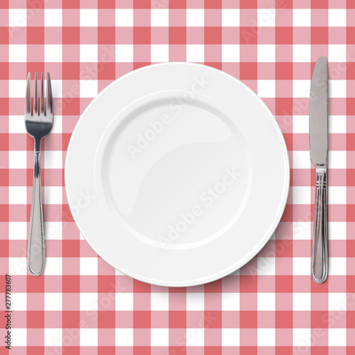 Close up view of empty white dish with knife and fork placed on classic checkered red tablecloth seamless background. View from above.