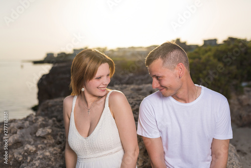 Happy young couple in love smiling by the sea at sunset.