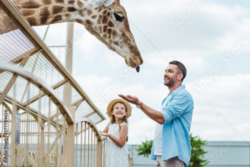 Canvas Print Selective focus of cheerful man gesturing while looking at giraffe near kid in z