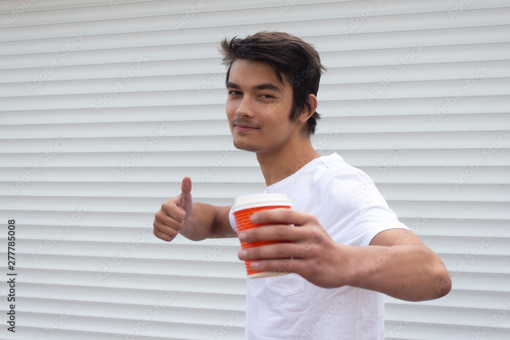 A young guy on a white background with a cup of coffee showing thumbs up. A young guy on a white background with a cup of coffee showing thumbs up.