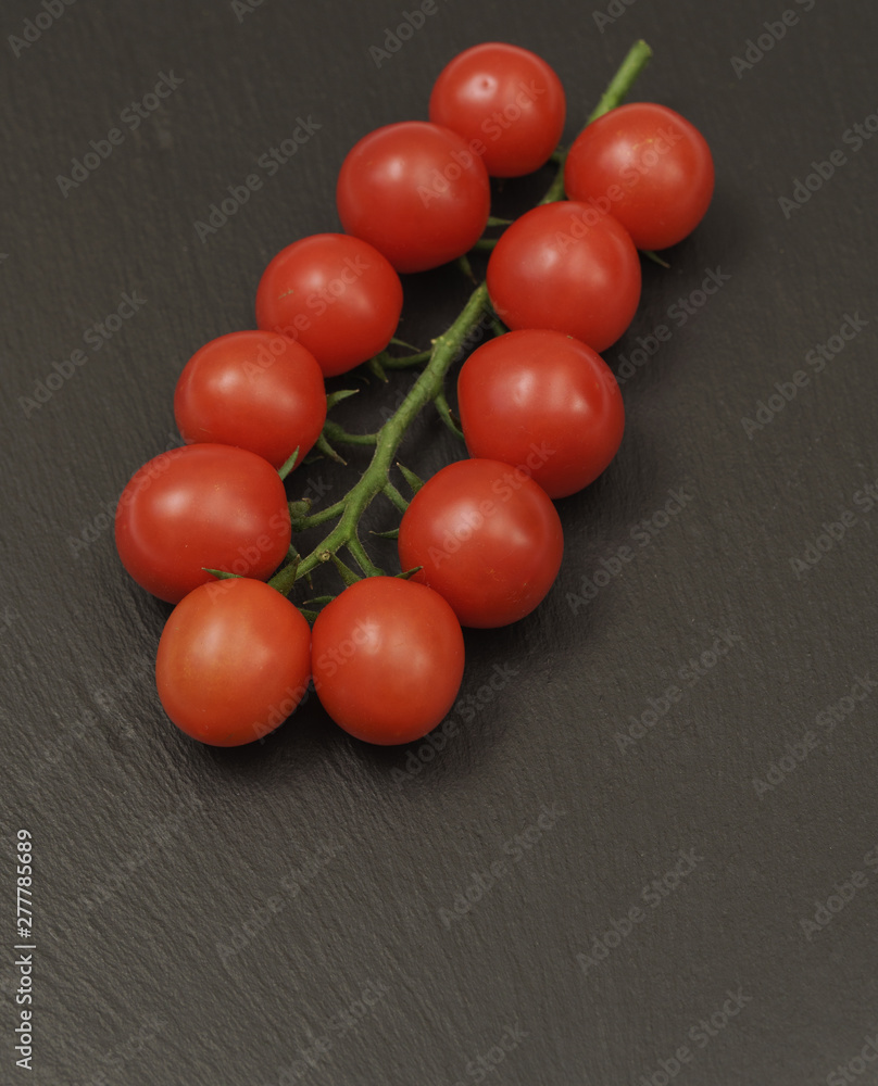 A branch of red cherry tomatoes on a dark slate background. Small and juicy vegetable is rich in vitamins and trace elements. Healthy food. Fresh and organic vegetables. Raw food A branch of red cherry tomatoes on a dark slate background. Small and juicy vegetable is rich in vitamins and trace elements. Healthy food. Fresh and organic vegetables. Raw food