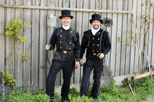 Portrait of two smiling chimney sweeps standing at wooden wall photo