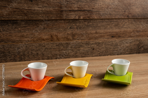 Side right to left inclined view of white coffee cups place on three colours plates.