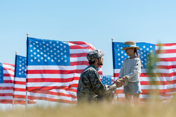 selective focus of military father holding hands with cheerful kid near american flags