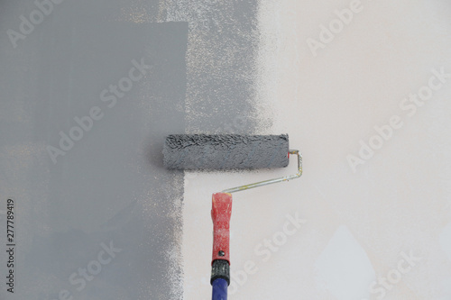 Paint roller. Painting with gray paint over a white wall