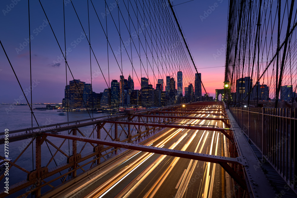 Obraz premium Most Brookliński z lekkimi szlakami i widokiem na Dolny Manhattan tuż po zachodzie słońca. Wieczór w Nowym Jorku, NY, USA