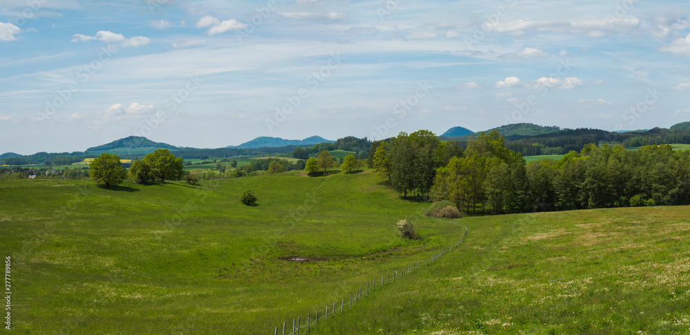 idyllic spring panoramic landscape in lucitian mountains, with lush green grass meadow, fresh deciduous and spruce tree forest, hills, blue sky white clouds background, horizontal, copy space