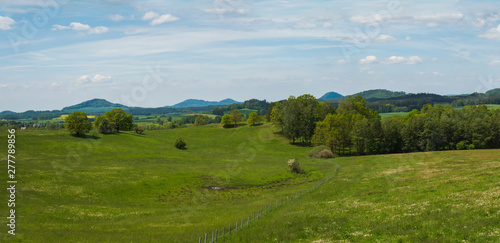 idyllic spring panoramic landscape in lucitian mountains  with lush green grass meadow  fresh deciduous and spruce tree forest  hills  blue sky white clouds background  horizontal  copy space
