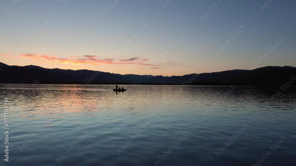 Flying low over a lake at dusk past small fishing boat as person reels in their pole at dusk in Montana. Flying low over a lake at dusk past small fishing boat as person reels in their pole at dusk in Montana.