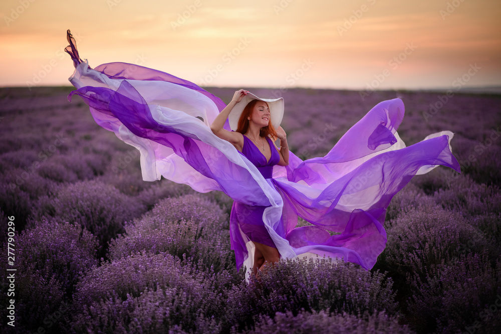 Young happy woman in luxurious purple dress standing in lavender field - obrazy, fototapety, plakaty 