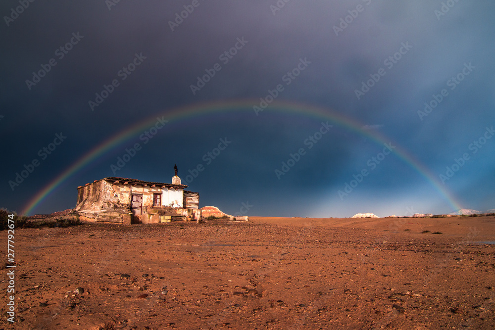 Lonely house in desert and rainbow in sky