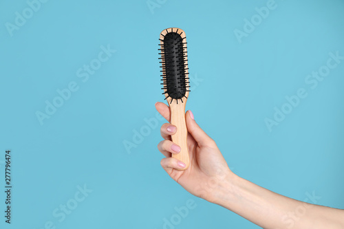 Woman holding wooden hair brush against blue background, closeup. Space for text
