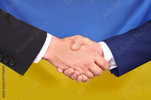 Men shaking hands against Ukrainian national flag, closeup. International relationships