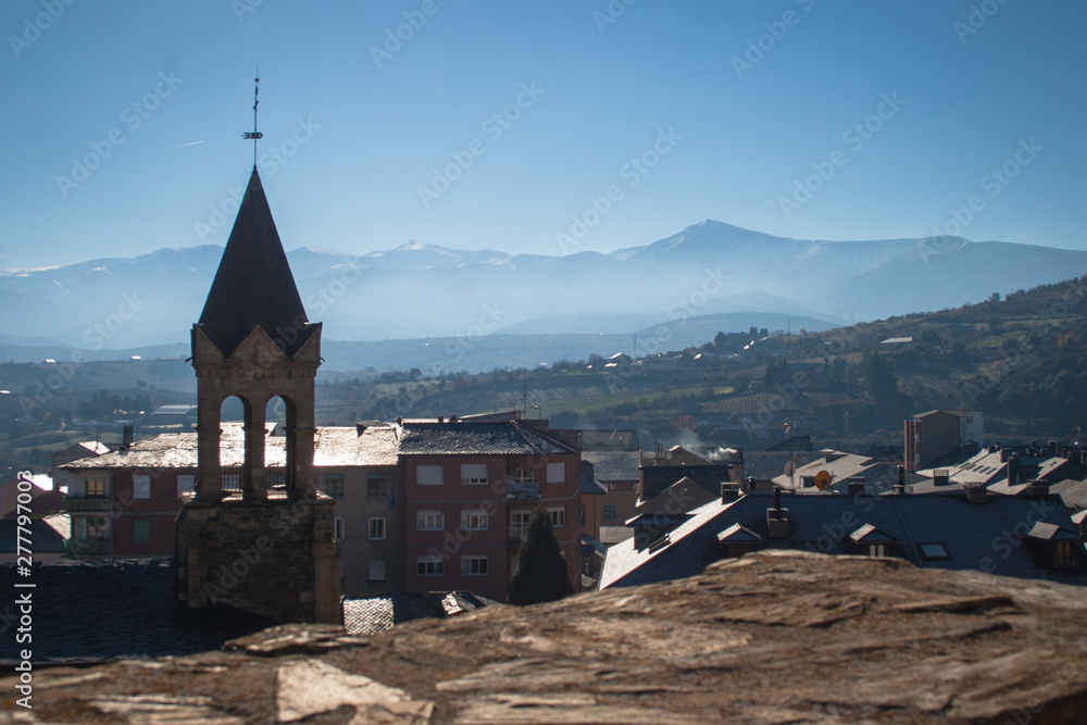 Tower and bell tower of the church of San Andres from the castle wall and Ponferrada, snowy mountains, fog and a blue sky background