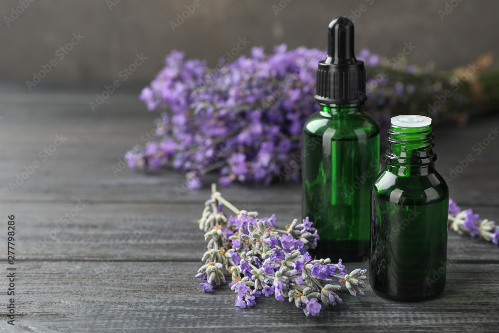 Bottles with natural lavender oil and flowers on wooden table against grey background, closeup view. Space for text Bottles with natural lavender oil and flowers on wooden table against grey background, closeup view. Space for text