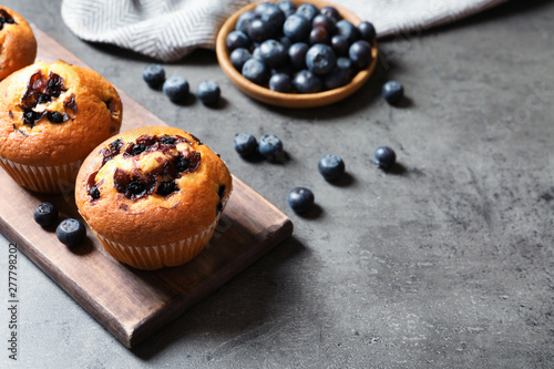 Wooden board with blueberry muffins on grey table, space for text