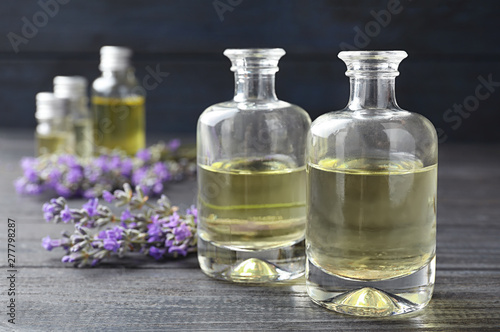 Bottles with natural lavender oil and flowers on grey wooden table against dark background, closeup view. Space for text