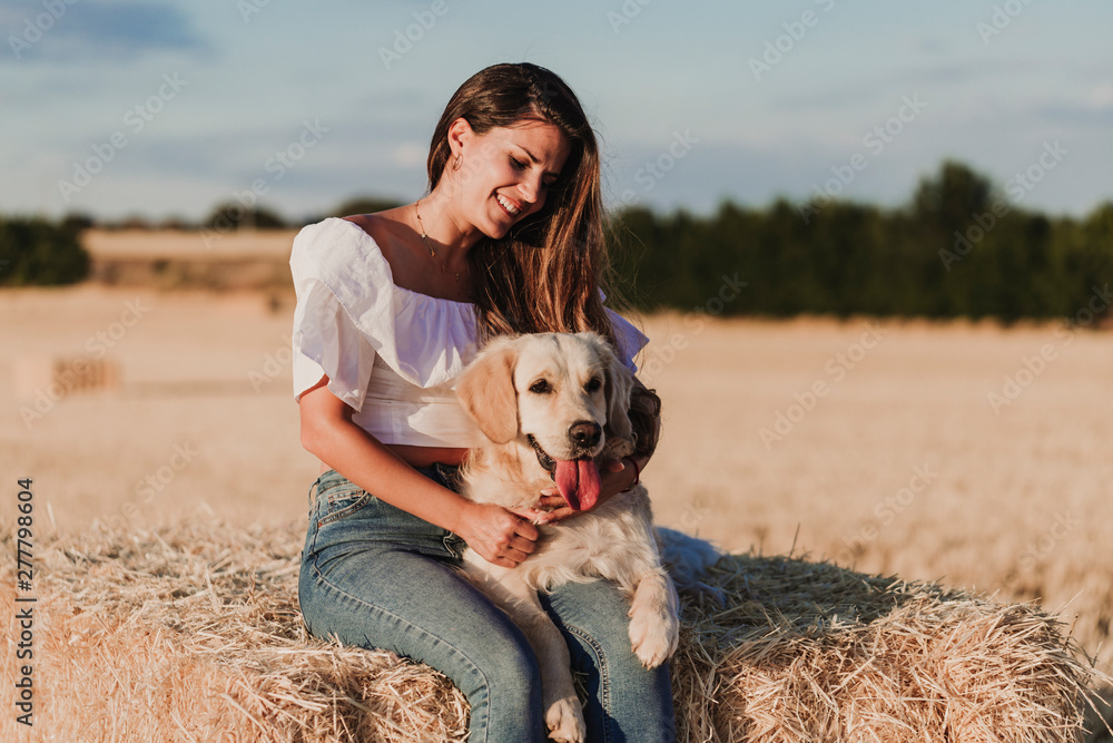 young beautiful woman walking with her golden retriever dog on a yellow field at sunset. Nature and lifestyle outdoors
