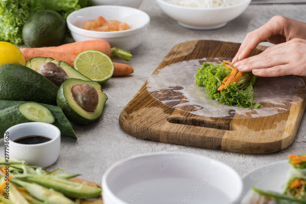 cropped view of woman putting cut carrot on lettuce and rice paper on cutting board cropped view of woman putting cut carrot on lettuce and rice paper on cutting board
