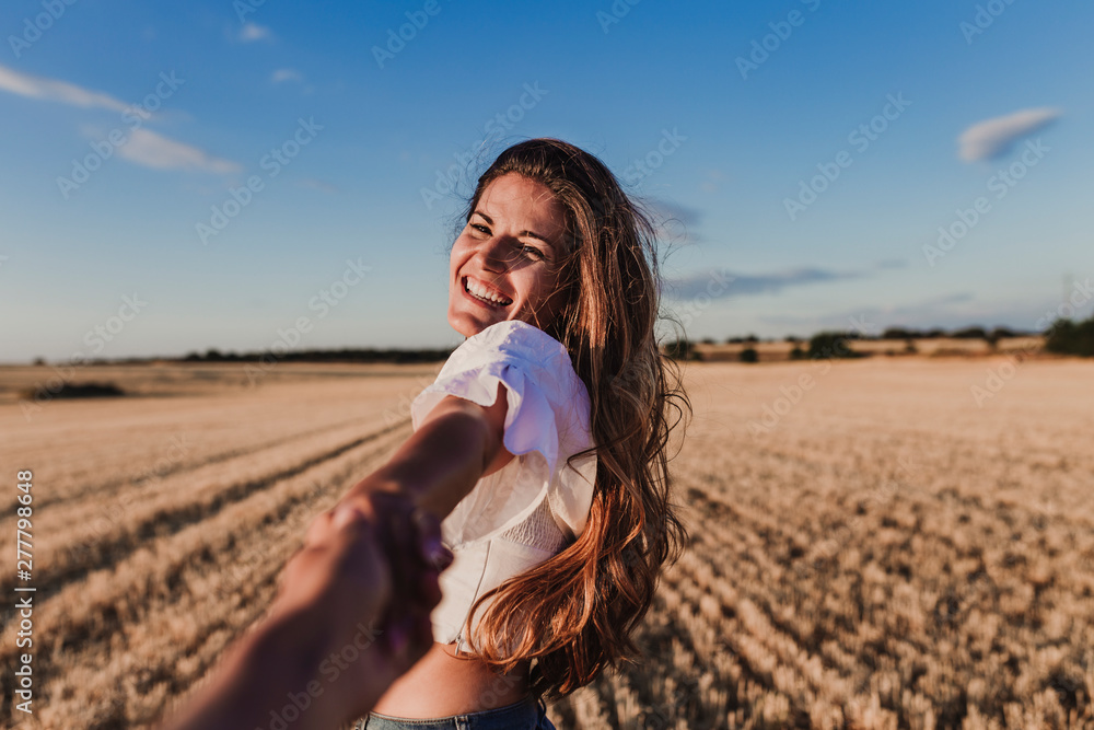 Follow me. Young woman holding hand and leading man to the beautiful nature sunset yellow landscape. View from back side, POV. Romantic couple travel, spend summer vacation together outdoors. - obrazy, fototapety, plakaty 