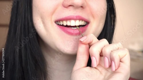 Young brunette woman eats red sweet cherry. Close-up.