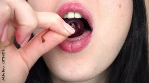 Young brunette woman eats red sweet cherry. Close-up.