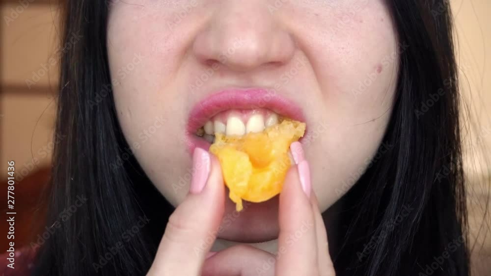 A young brunette woman is eating a small juicy peach. Close-up. A young brunette woman is eating a small juicy peach. Close-up.