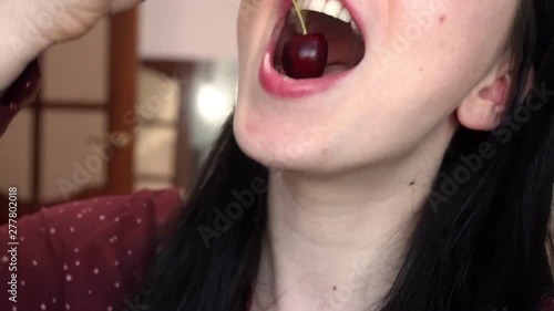 Young brunette woman eats red sweet cherry. Close-up.