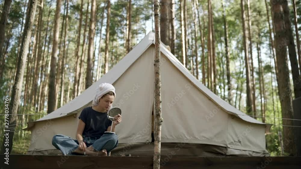 Woman puts on make-up near the tent and looking at mirror. Woman puts on make-up near the tent and looking at mirror.