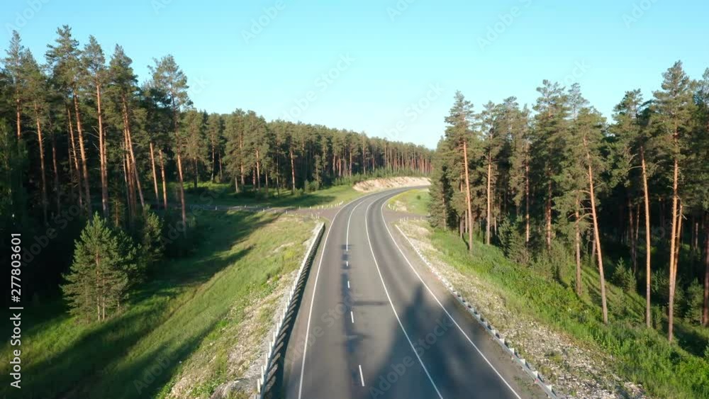 The camera follows the road between the pine forest.Aerial follow shot.Cars passing by.Type 2 The camera follows the road between the pine forest.Aerial follow shot.Cars passing by.Type 2