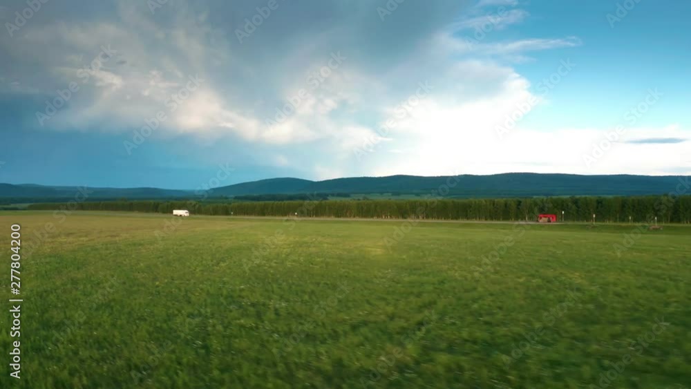 White truck driving on the highway.Beautiful nature around.Road between the fields and forest belt. Mountains in the background.Cloudy day in the evening golden hours. White truck driving on the highway.Beautiful nature around.Road between the fields and forest belt. Mountains in the background.Cloudy day in the evening golden hours.