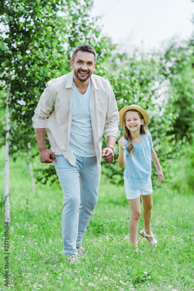 cute and happy kid in straw hat gesturing near cheerful father looking at camera