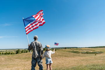 Back view of military father and patriotic kid holding American flags