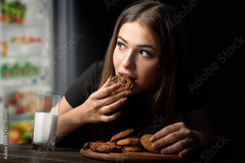 woman eats sweets at night to sneak in a refrigerator