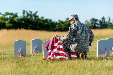 man in military uniform and cap holding american flag while sitting in graveyard