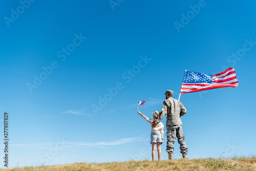 Foto Back view of child in straw hat and military father holding American flags while