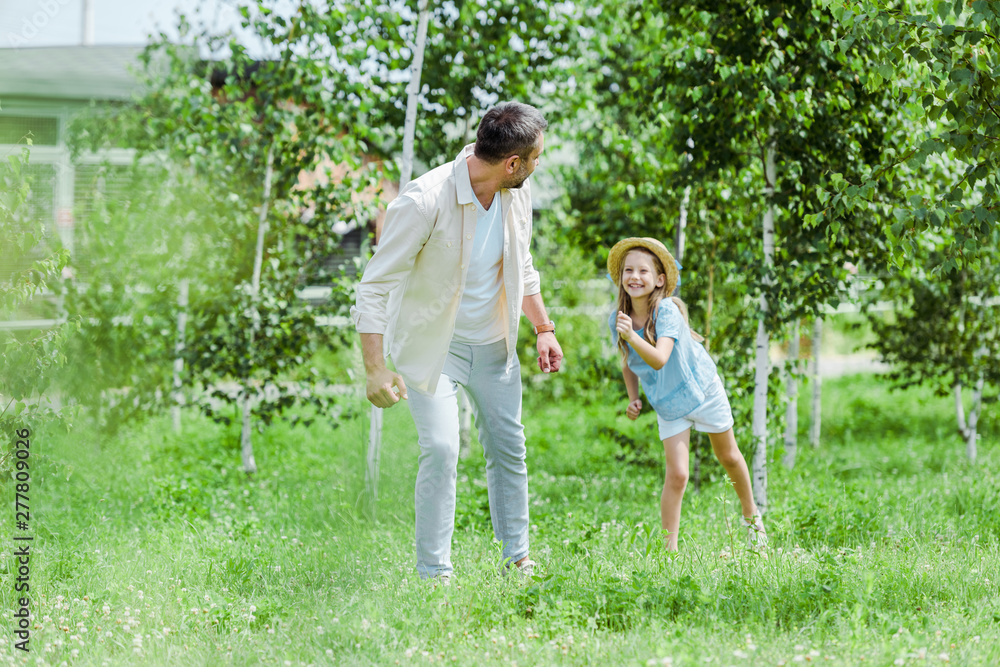 selective focus of happy kid gesturing while looking at father and standing on grass selective focus of happy kid gesturing while looking at father and standing on grass