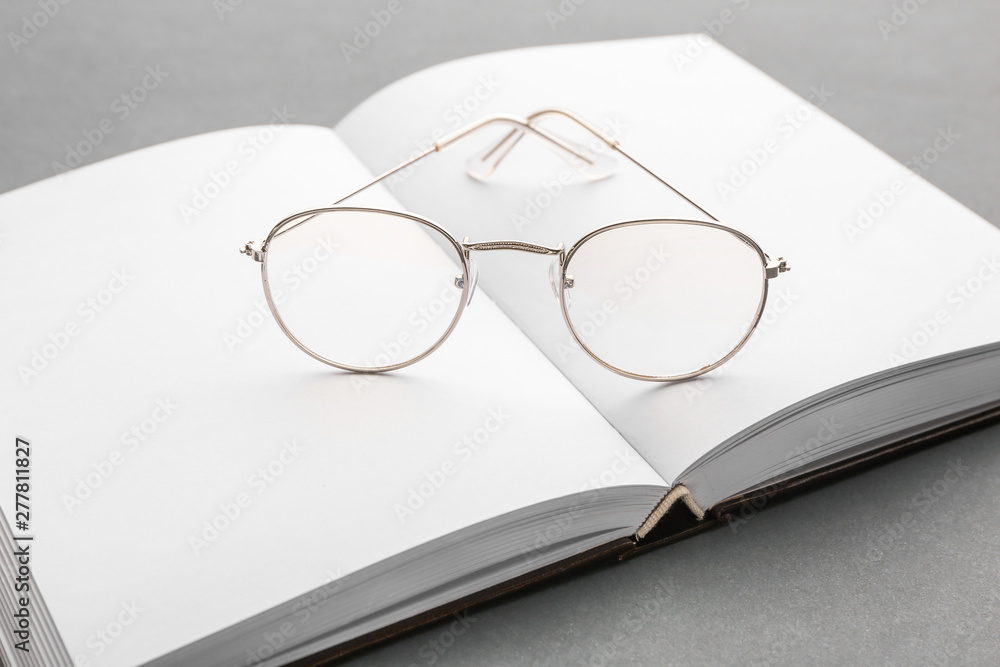 Open book with eyeglasses on grey background Open book with eyeglasses on grey background