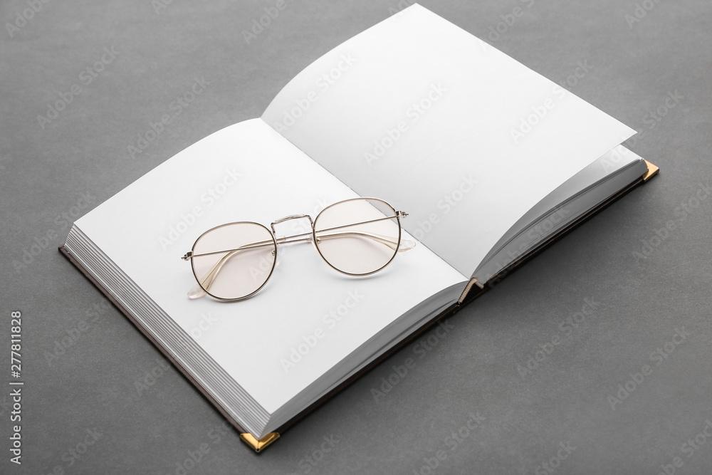 Open book with eyeglasses on grey background Open book with eyeglasses on grey background