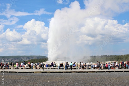 Old Faithful erupts on a beautiful summer day in front of a crowd of onlookers