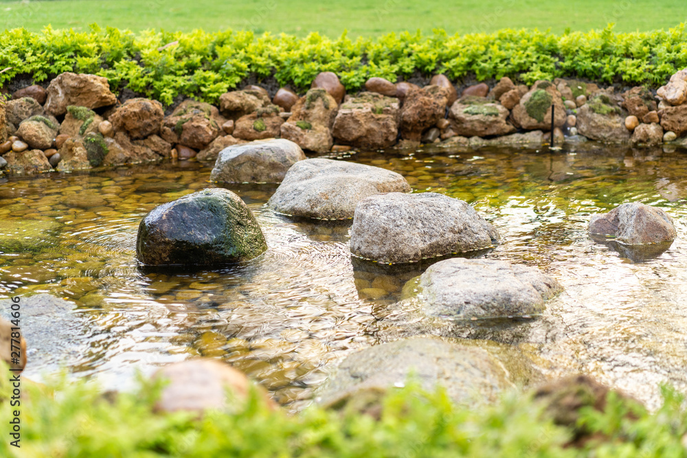 Stone in the small steaming river created by human at garden in the sunshine day. Stone in the small steaming river created by human at garden in the sunshine day.