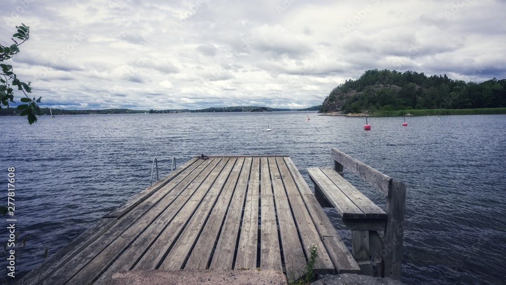 Fototapeta premium Old wooden pier. Empty berth on the Baltic sea coast. Dramatic cloudy sky. Horizon. Vintage Picture. Seascape: amazing view. Beautiful picture of sea coast line in Scandinavia. Empty jetty on cloudy d