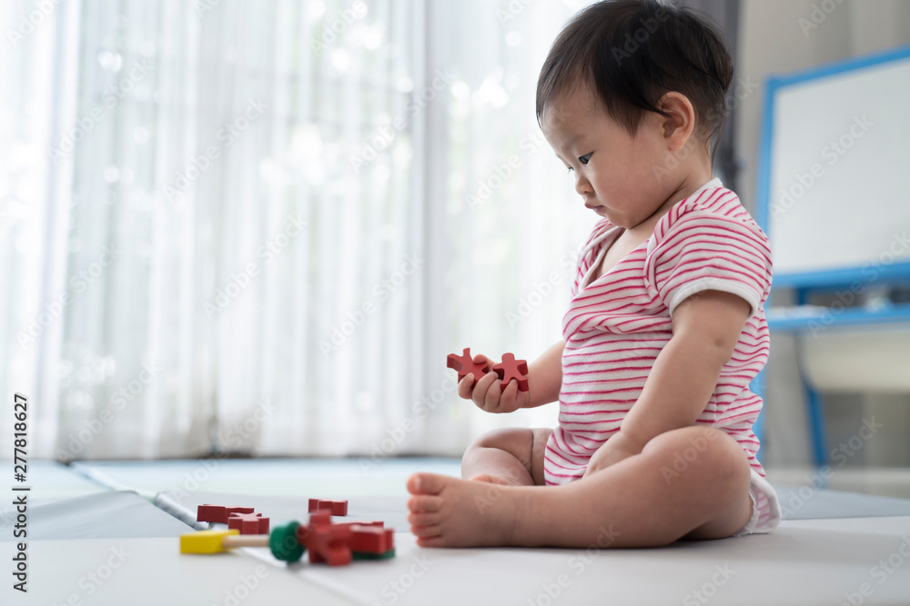Asian cute baby sitting and playing a small toy on soft mat at home. The kid holding the toy and question about how to play it. Play and learn of young child education concept. Seen from child side. Asian cute baby sitting and playing a small toy on soft mat at home. The kid holding the toy and question about how to play it. Play and learn of young child education concept. Seen from child side.